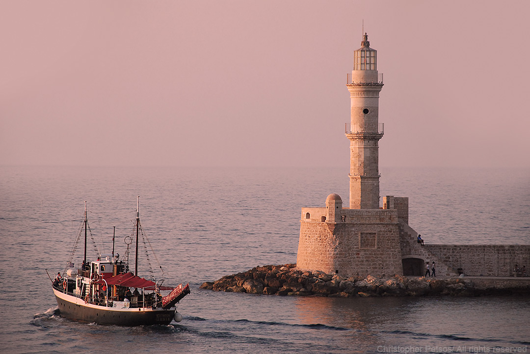 old lighthouse on a harbor in Crete with a boat on the water and soft pink light