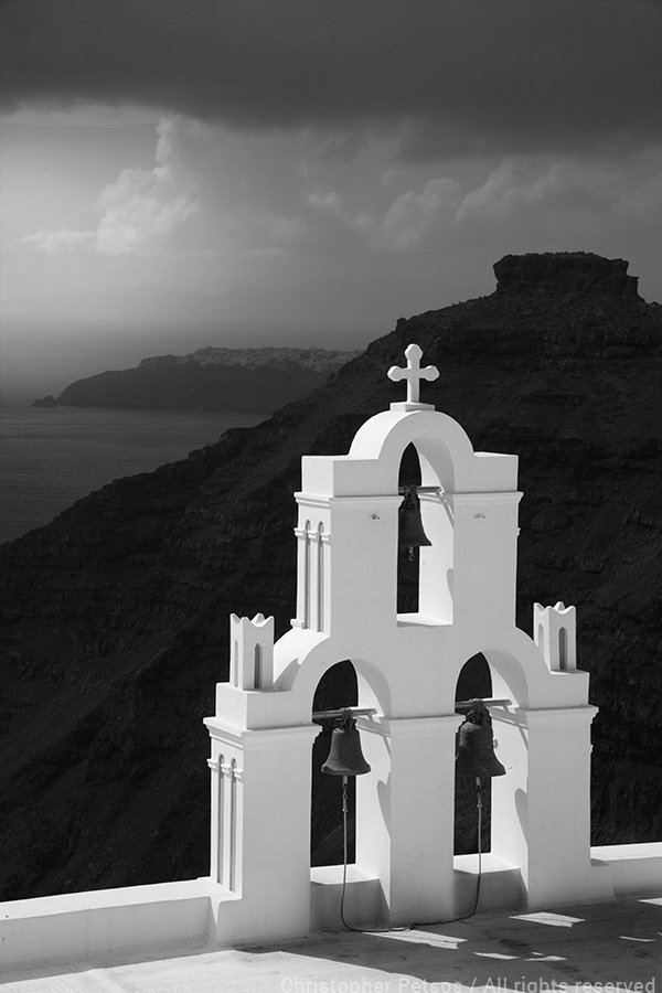 Black and white photo of a white church belfry above cliffs and water with a dramatic sky