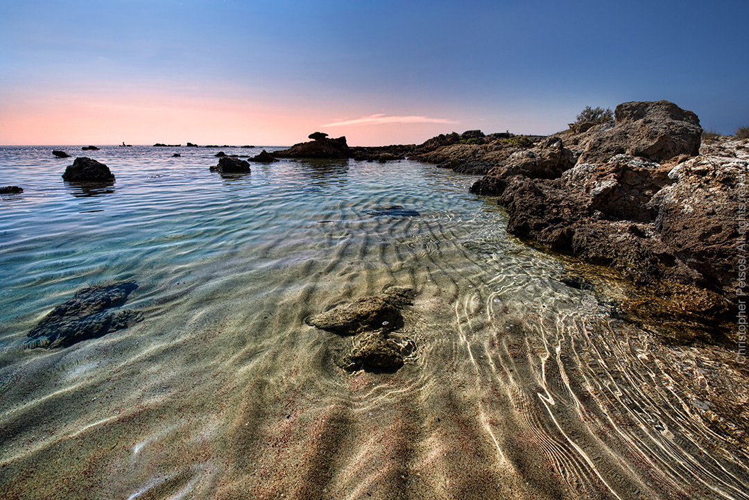 clear water with ripples and rocks as the sun sets