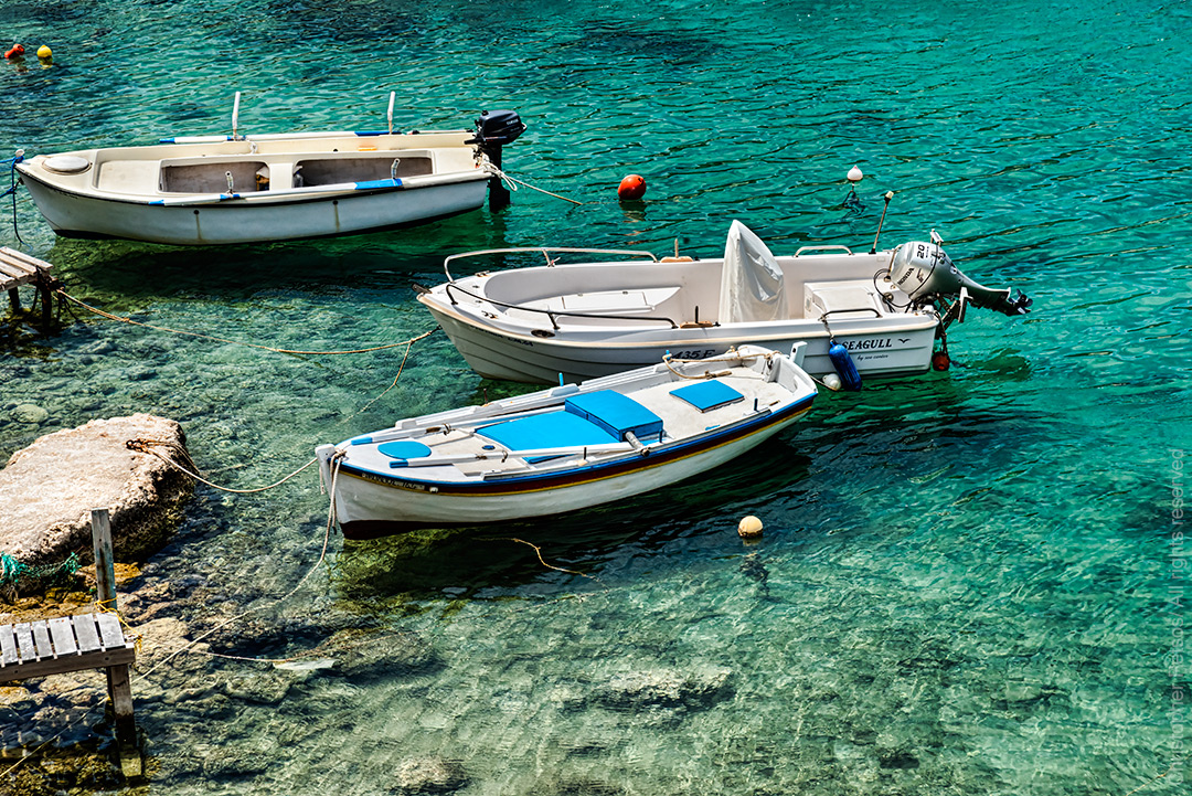 Three white fishing boats float in shallow clear turquoise water