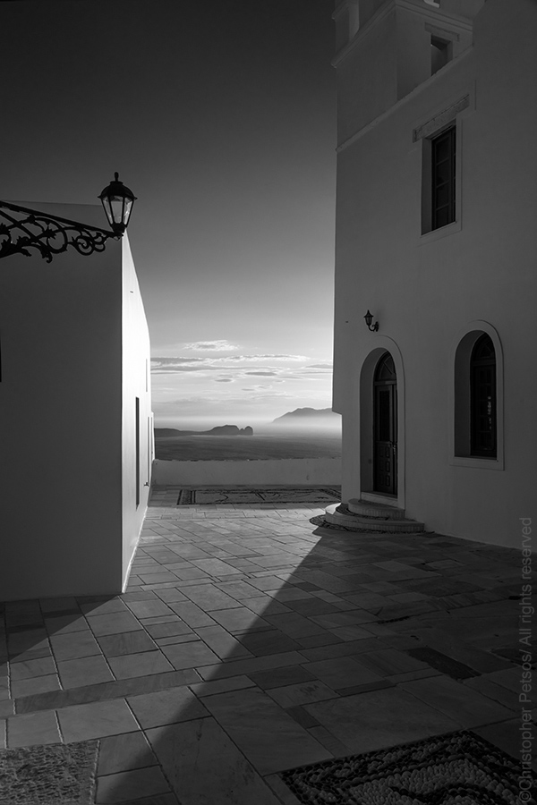 dramatic black and white of a small plaza overlooking the sea in Milos by Christopher Petsos