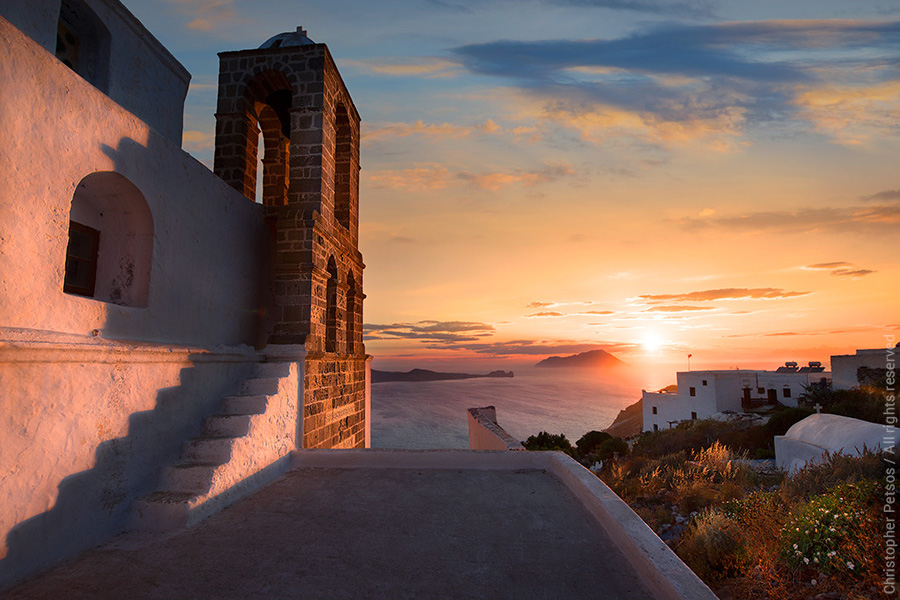 Sunset casting dramatic shadows on a church steeple and stairs above the water in Milos, Greece