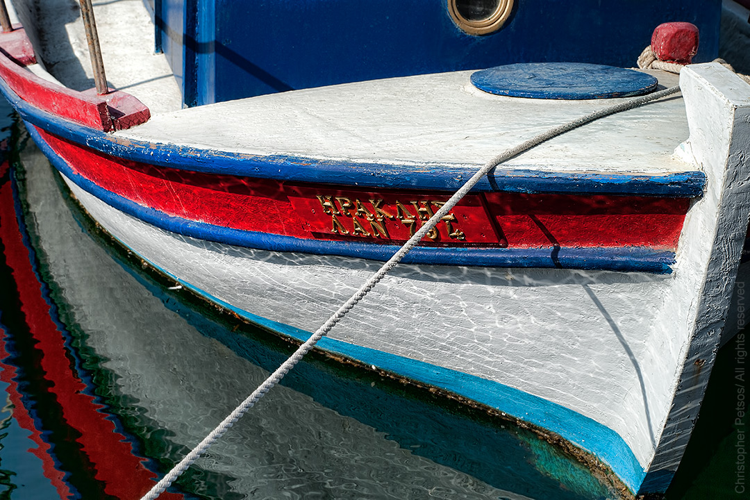 Close up of a colorful fishing boat with reflections on the water in Crete, Greece by Chris Petsos