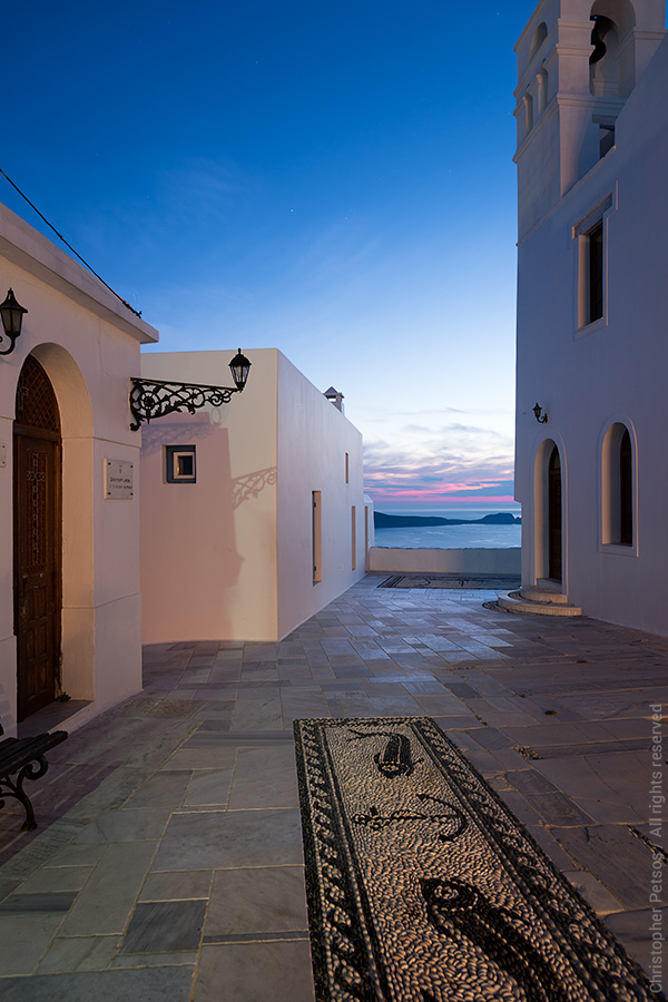 Greek village square above water with pebble mosaic at night and cycladic architecture
