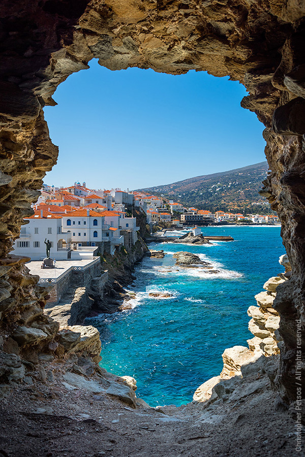 Fine art photo print of the view over Andros, Greece looking through the ruins of the old Venetian castle with a town on the water 