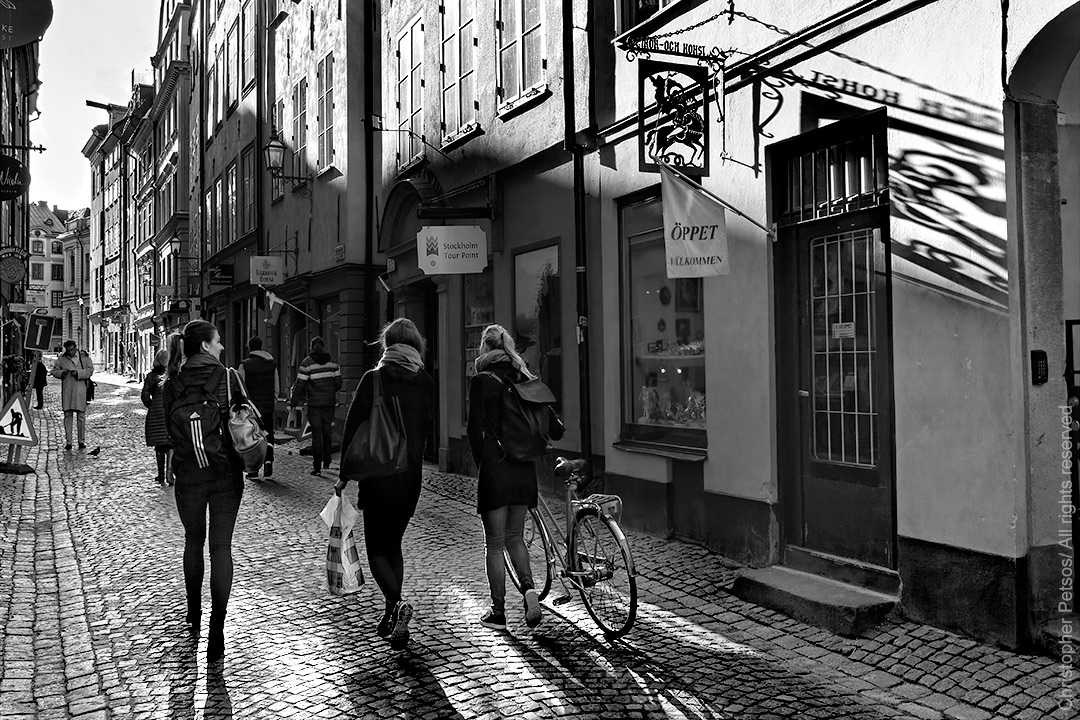 three Stockholm women walking along a cobblestone street with shadows and architecture