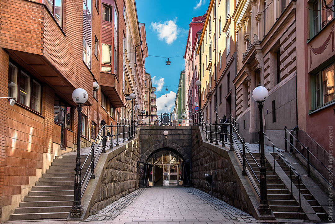 Street in Stockholm with stairs on each side, light posts, colorful architecture and a tunnel entrance